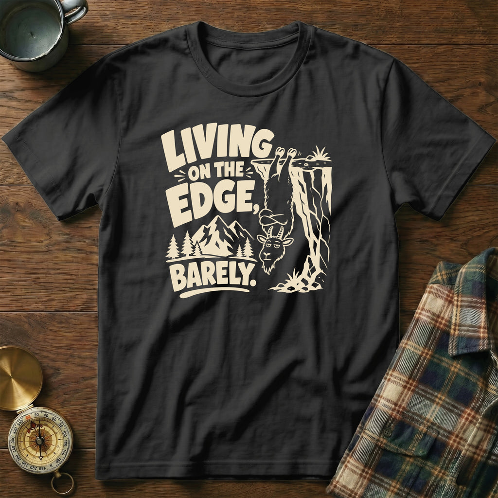 Black t-shirt with text "LIVING ON THE EDGE, BARELY" and a goat hanging off a cliff.