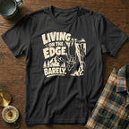 Black t-shirt with text "LIVING ON THE EDGE, BARELY" and a goat hanging off a cliff.