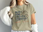 T-shirt with "Built for Uneven Terrain" text and mountain graphic.