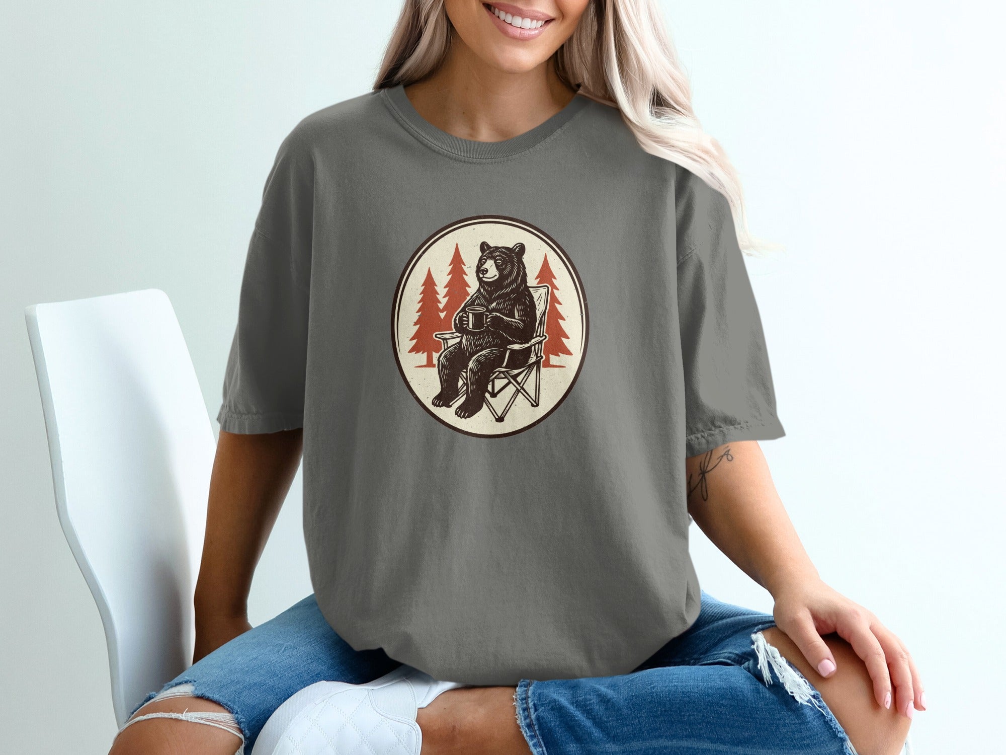 Bear sitting in a chair with a mug and trees in oval graphic on a t-shirt.