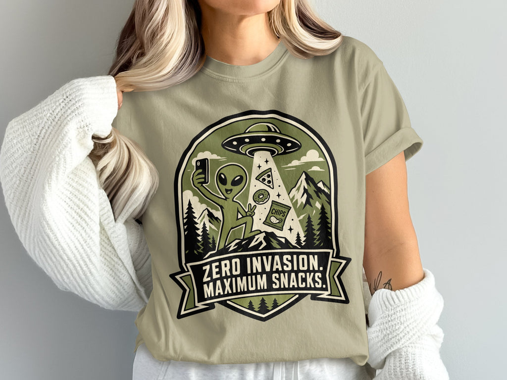 Alien on a t-shirt taking a selfie with a UFO, pizza, donut, and chips.