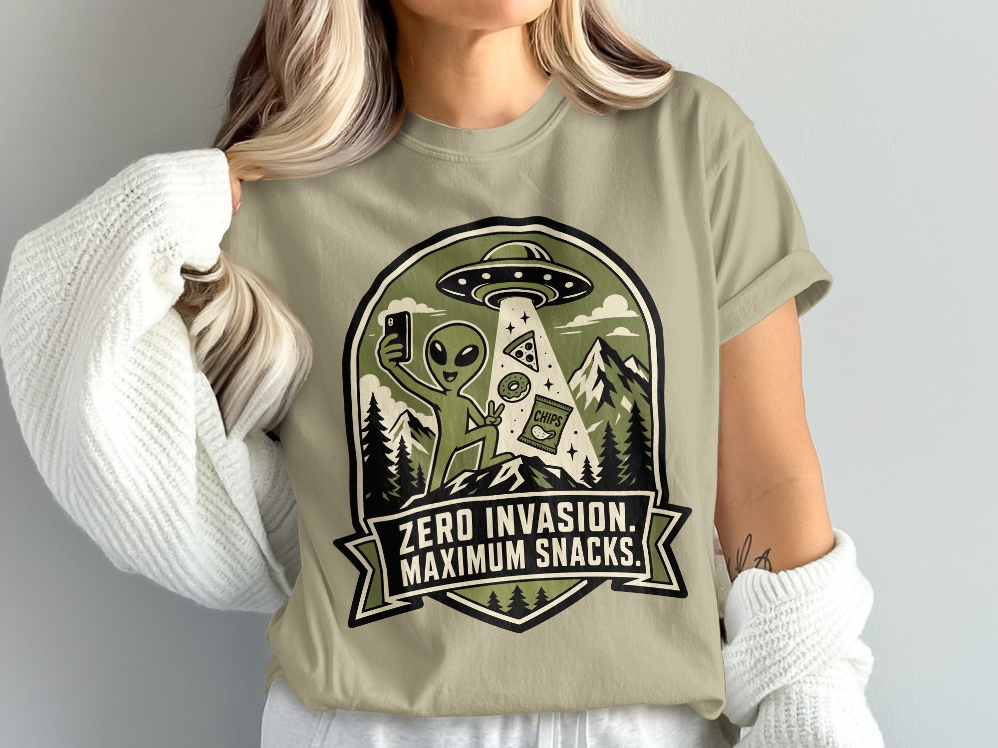 Alien on a t-shirt taking a selfie with a UFO, pizza, donut, and chips.
