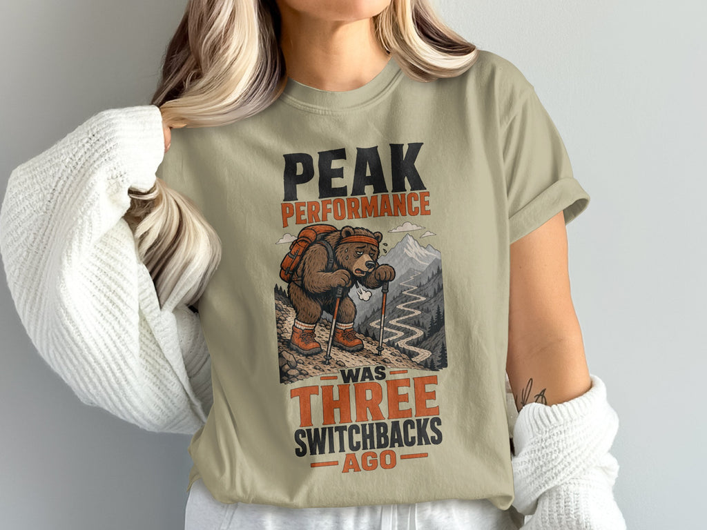 T-shirt graphic of a bear hiking, with text "Peak Performance Was Three Switchbacks Ago".
