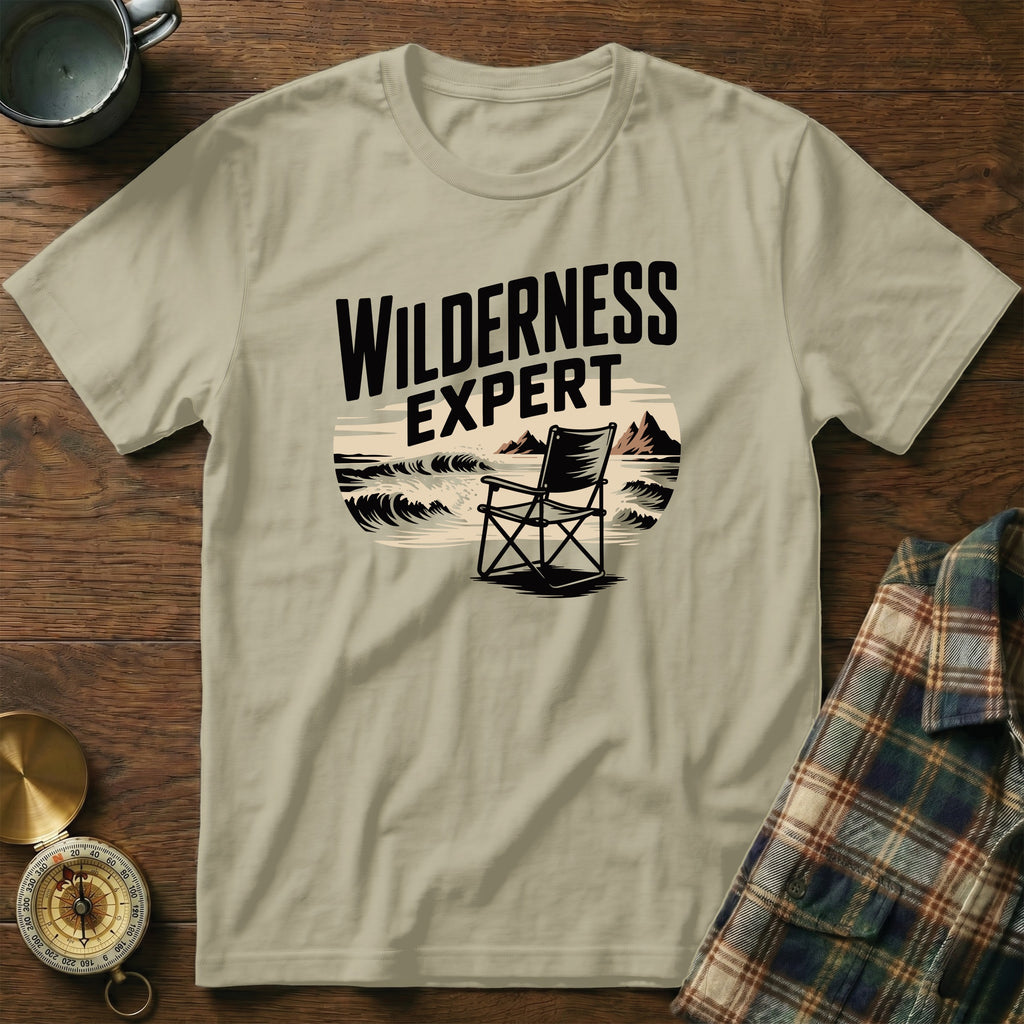 T-shirt with "WILDERNESS EXPERT" text above a camp chair by the sea.