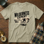 T-shirt with "WILDERNESS EXPERT" text above a camp chair by the sea.