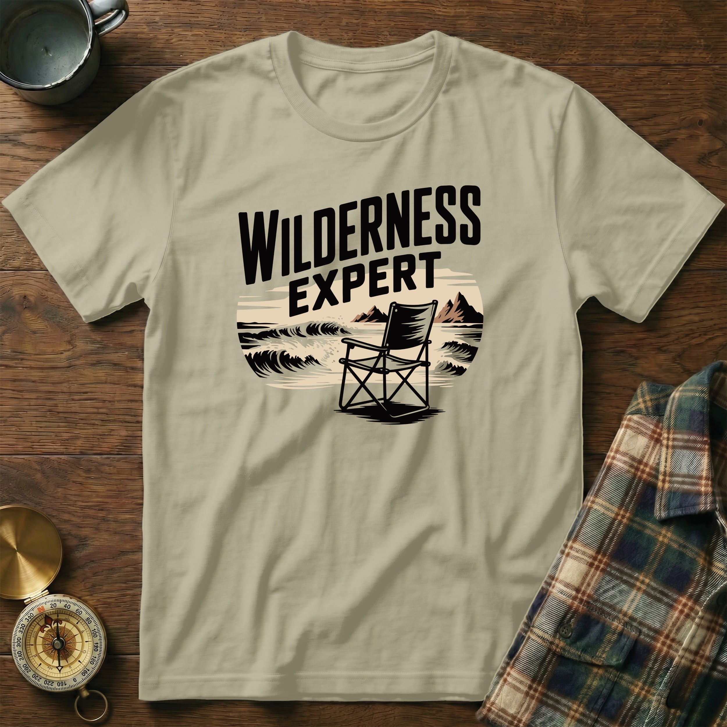 T-shirt with "WILDERNESS EXPERT" text above a camp chair by the sea.