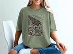 Osprey catching fish in waves, woodcut style graphic on olive green t-shirt.