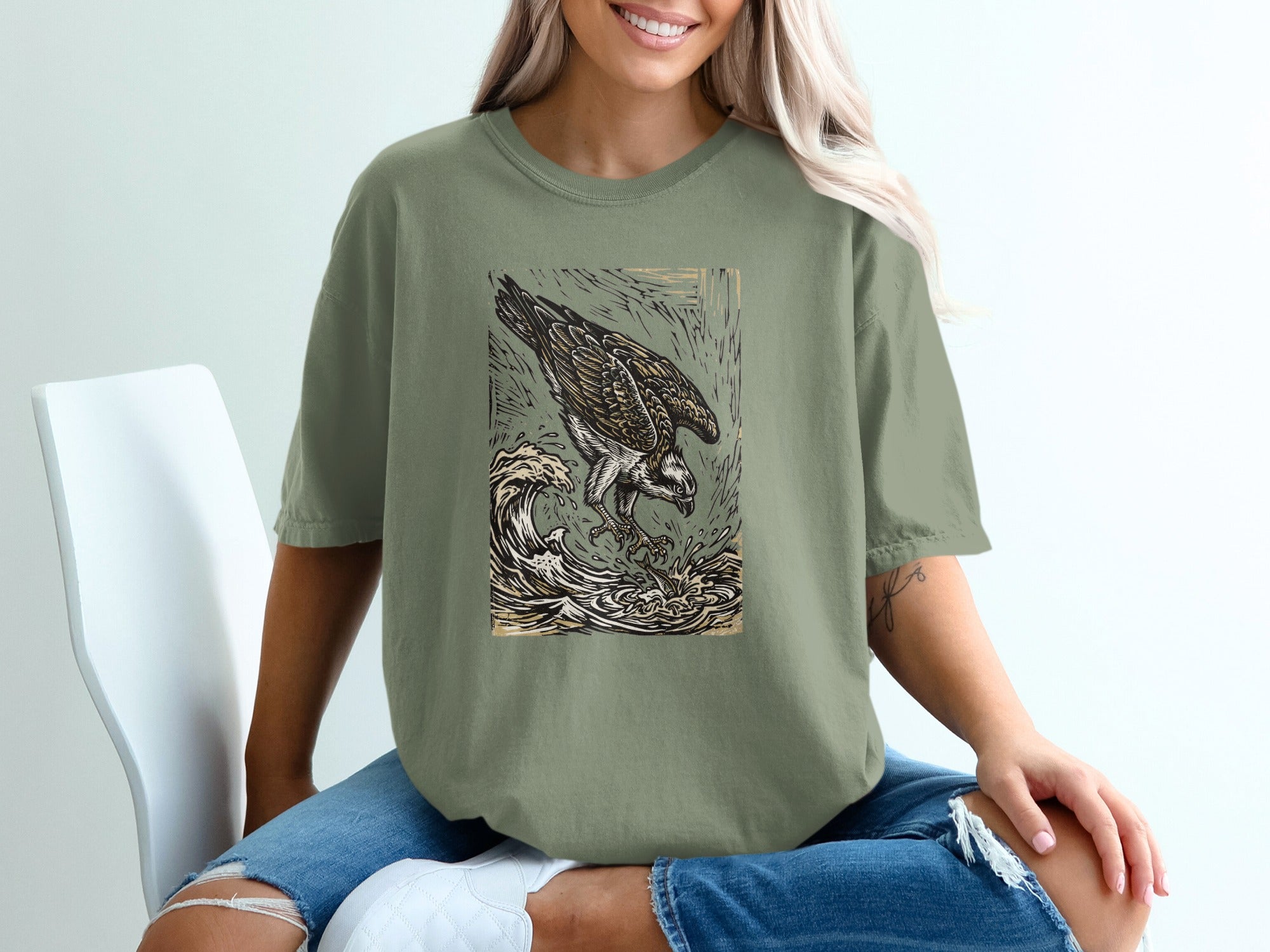Osprey catching fish in waves, woodcut style graphic on olive green t-shirt.