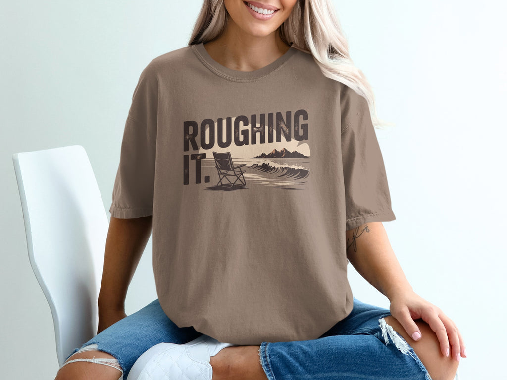 Brown t-shirt with "ROUGHING IT." text and a beach scene graphic.