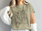 Light brown t-shirt with six postage stamp illustrations: compass, sailboat, crab, waves, grass, and lighthouse.