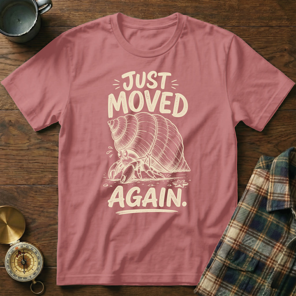 Pink t-shirt with a sketch of a hermit crab and text "JUST MOVED AGAIN."