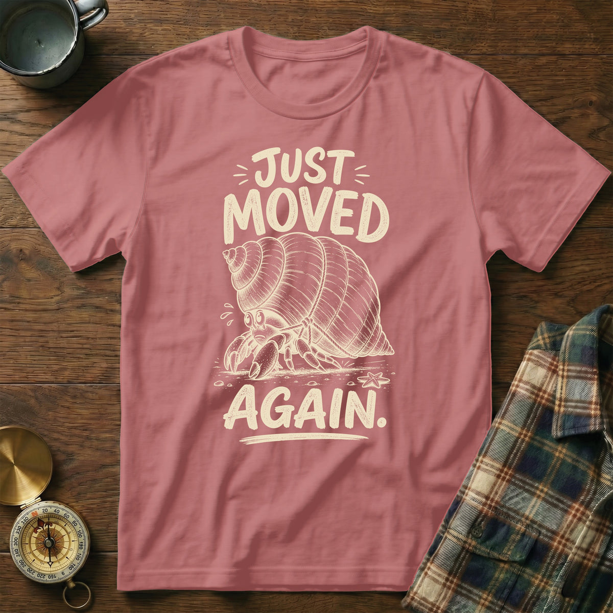 Pink t-shirt with a sketch of a hermit crab and text "JUST MOVED AGAIN."