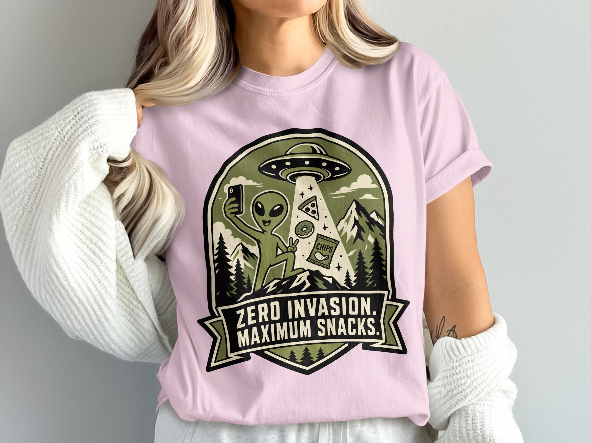 Alien taking a selfie with pizza, donut, and chips under a UFO, text reads "ZERO INVASION. MAXIMUM SNACKS."