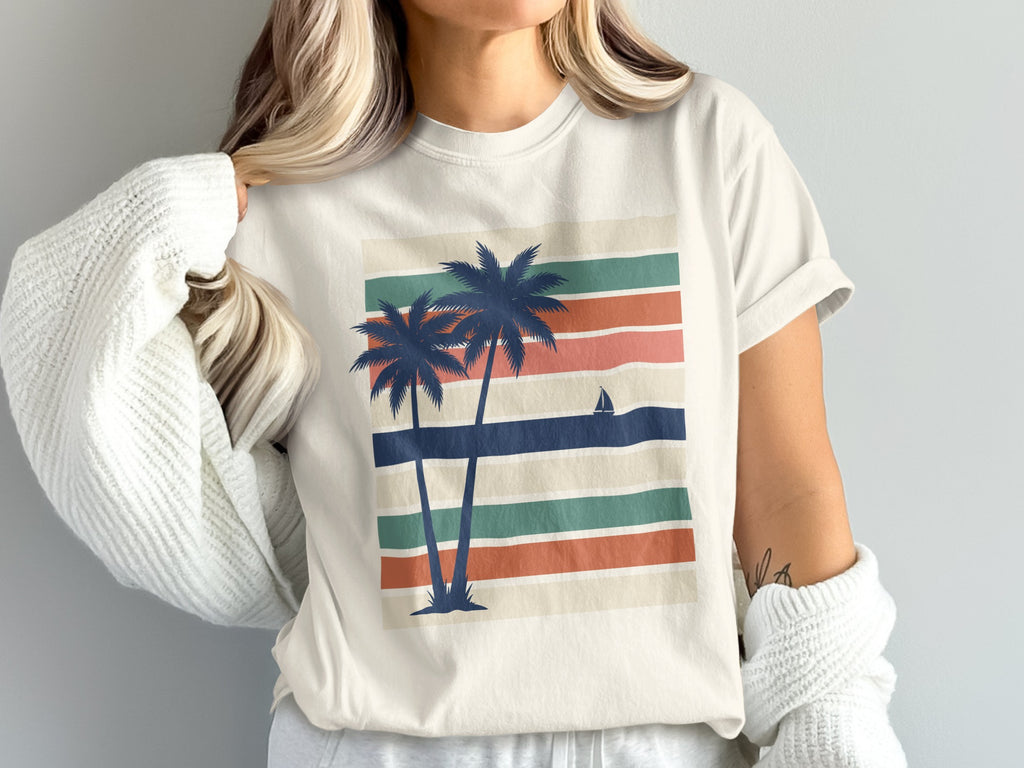 Cream t-shirt with retro palm trees and sailboat on striped background.