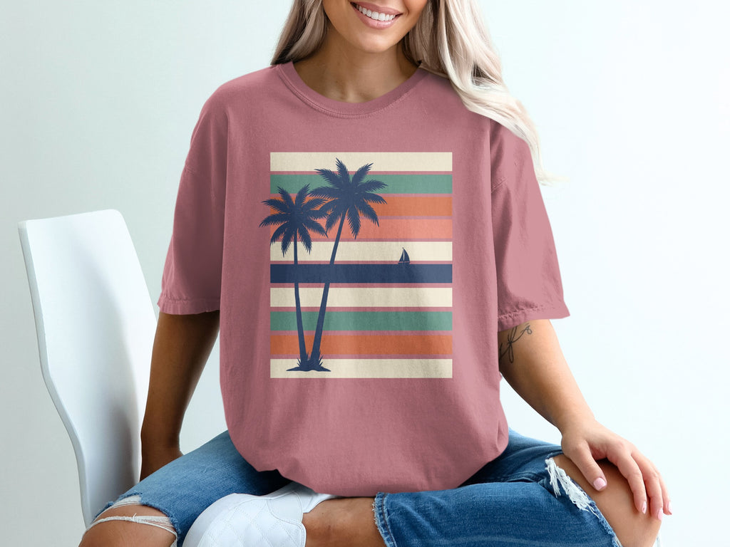 Pink t-shirt with palm trees and sailboat on striped background.