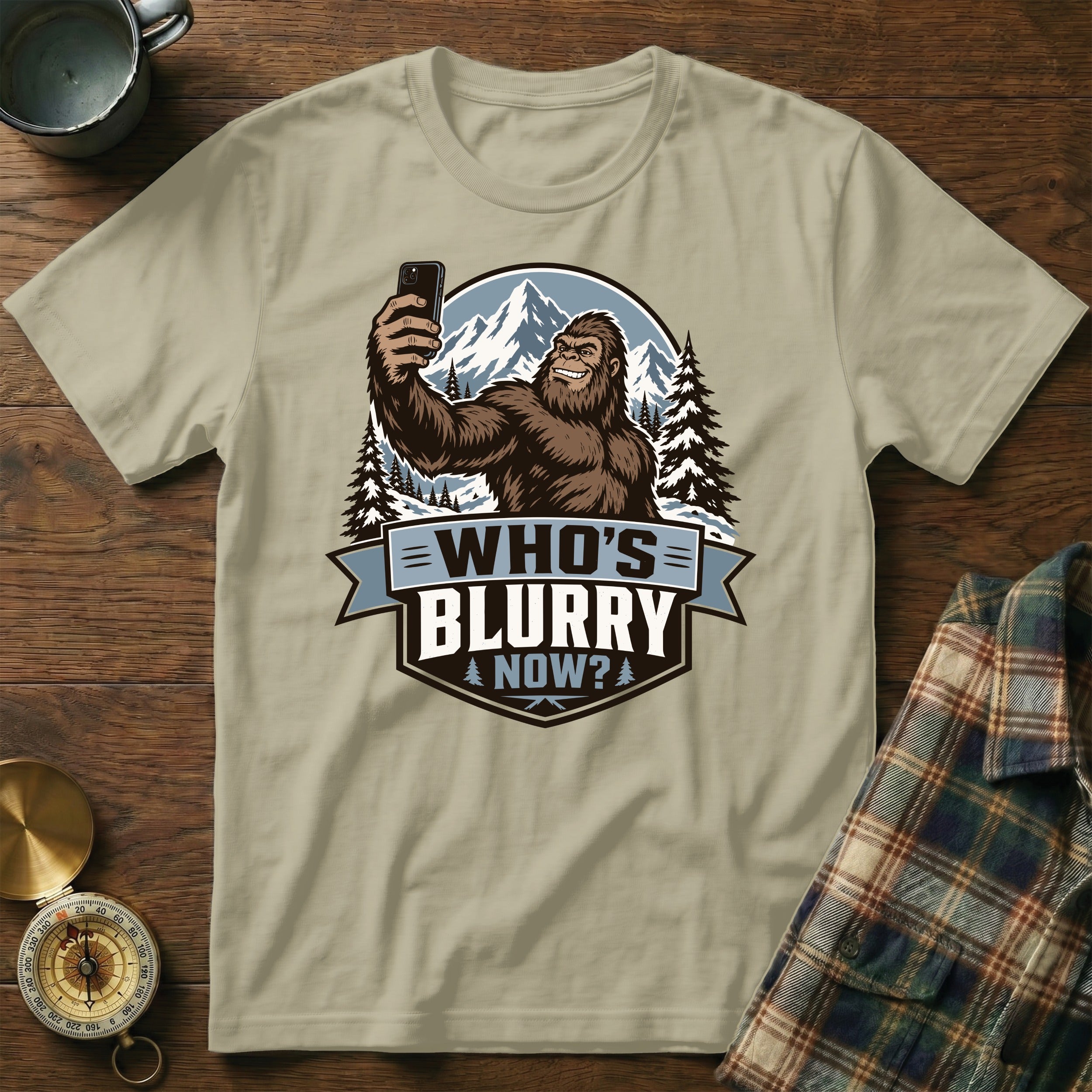 T-shirt graphic of Bigfoot taking a selfie with mountains and text "WHO'S BLURRY NOW?".