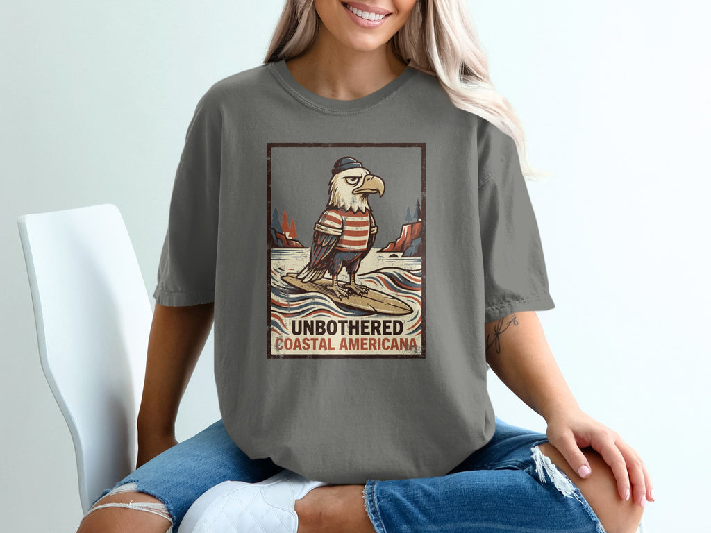 Graphic tee with eagle on surfboard, text "UNBOTHERED COASTAL AMERICANA".