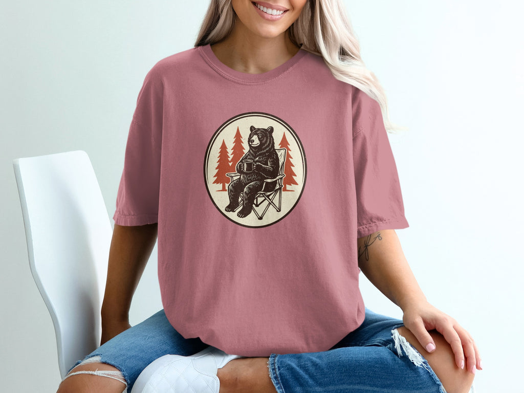 Bear sitting in a chair holding a mug with pine trees in the background.