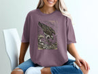 Osprey in flight over crashing waves, stylized graphic on a mauve t-shirt.
