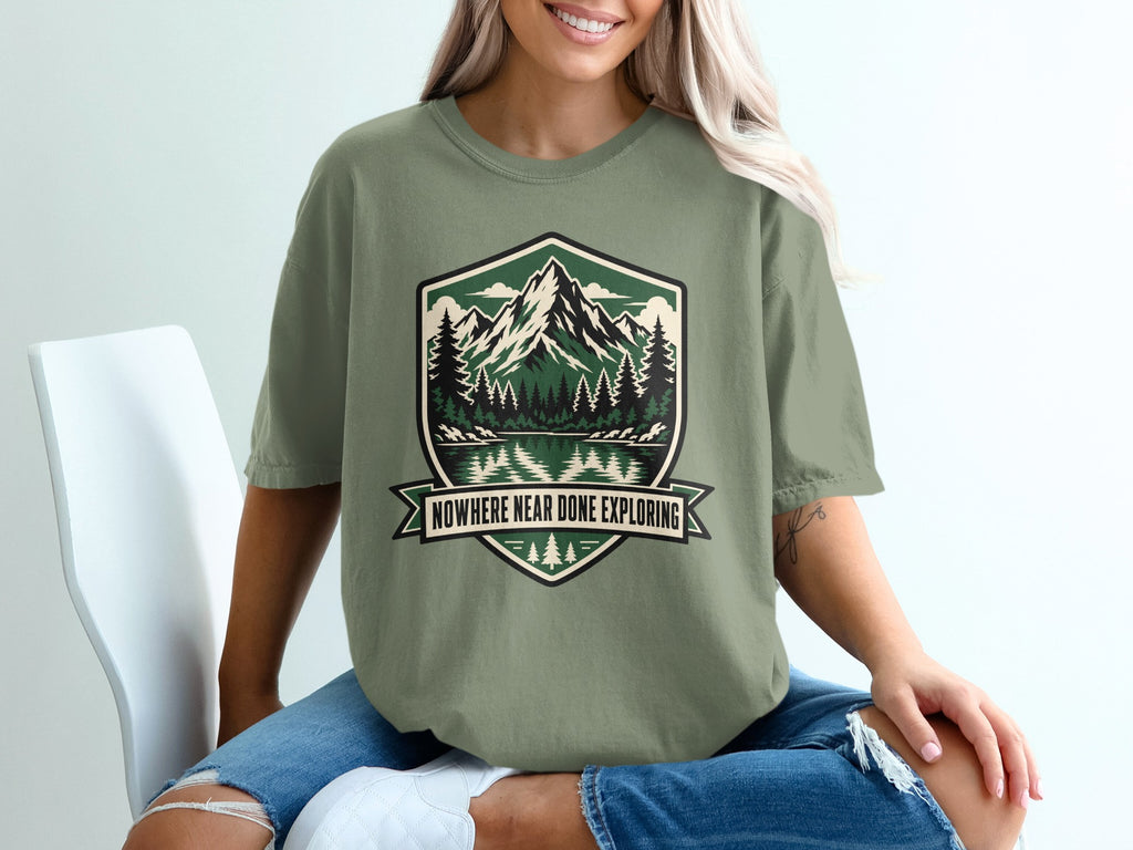 Olive green t-shirt with mountain, forest, and lake art and text "Nowhere Near Done Exploring."