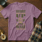 Mauve short-sleeve t-shirt with green text reading HURRY UP AND WAIT and an hourglass graphic.