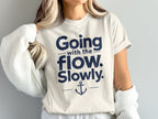 A person wearing a cream-colored t-shirt featuring the blue text Going with the flow. Slowly. and an anchor graphic.