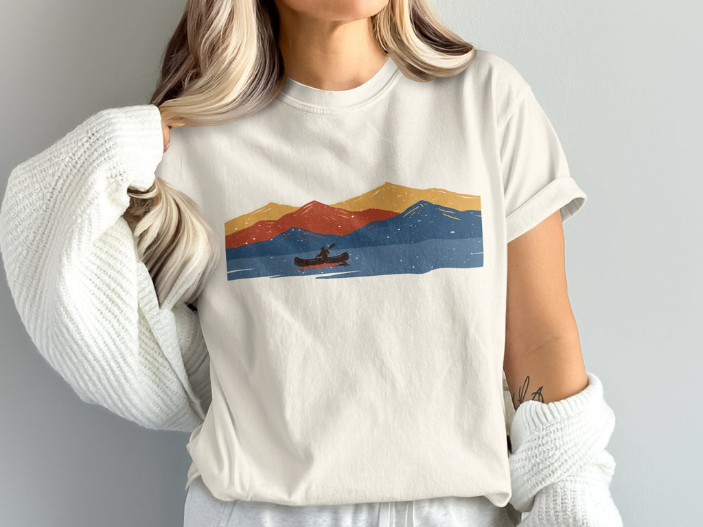 T-shirt graphic with canoeist on water and colorful mountains under speckled sky.