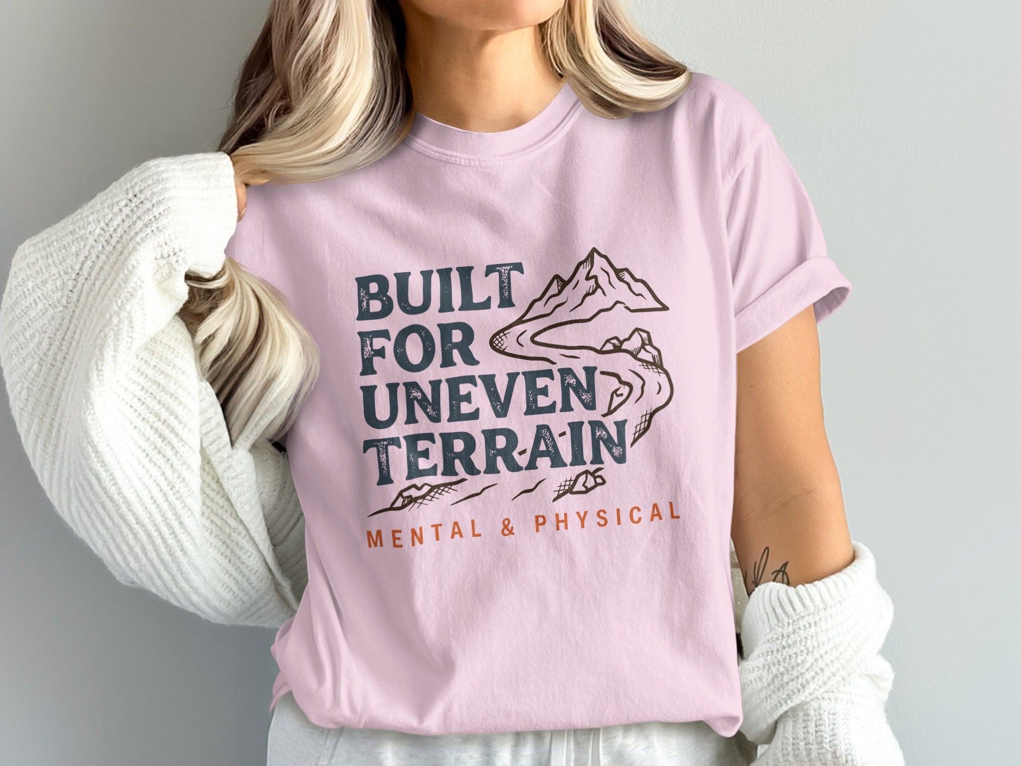 Pink t-shirt with mountains, river, and text "Built for Uneven Terrain".