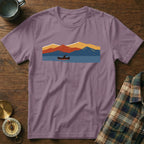 Purple t-shirt with a graphic of a canoe on a lake with colorful mountains.