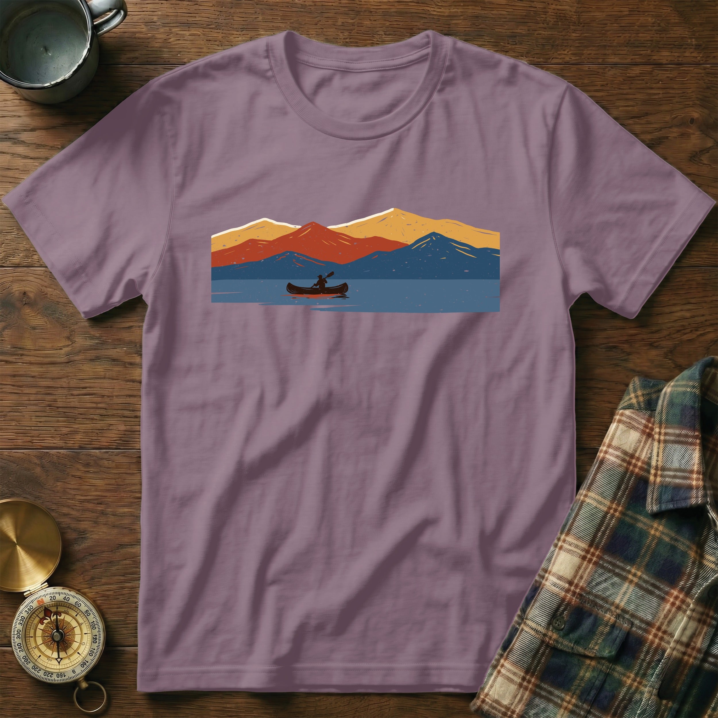 Purple t-shirt with a graphic of a canoe on a lake with colorful mountains.