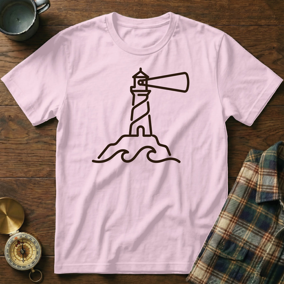 Pink t-shirt with a black outline drawing of a lighthouse on rocks with waves.