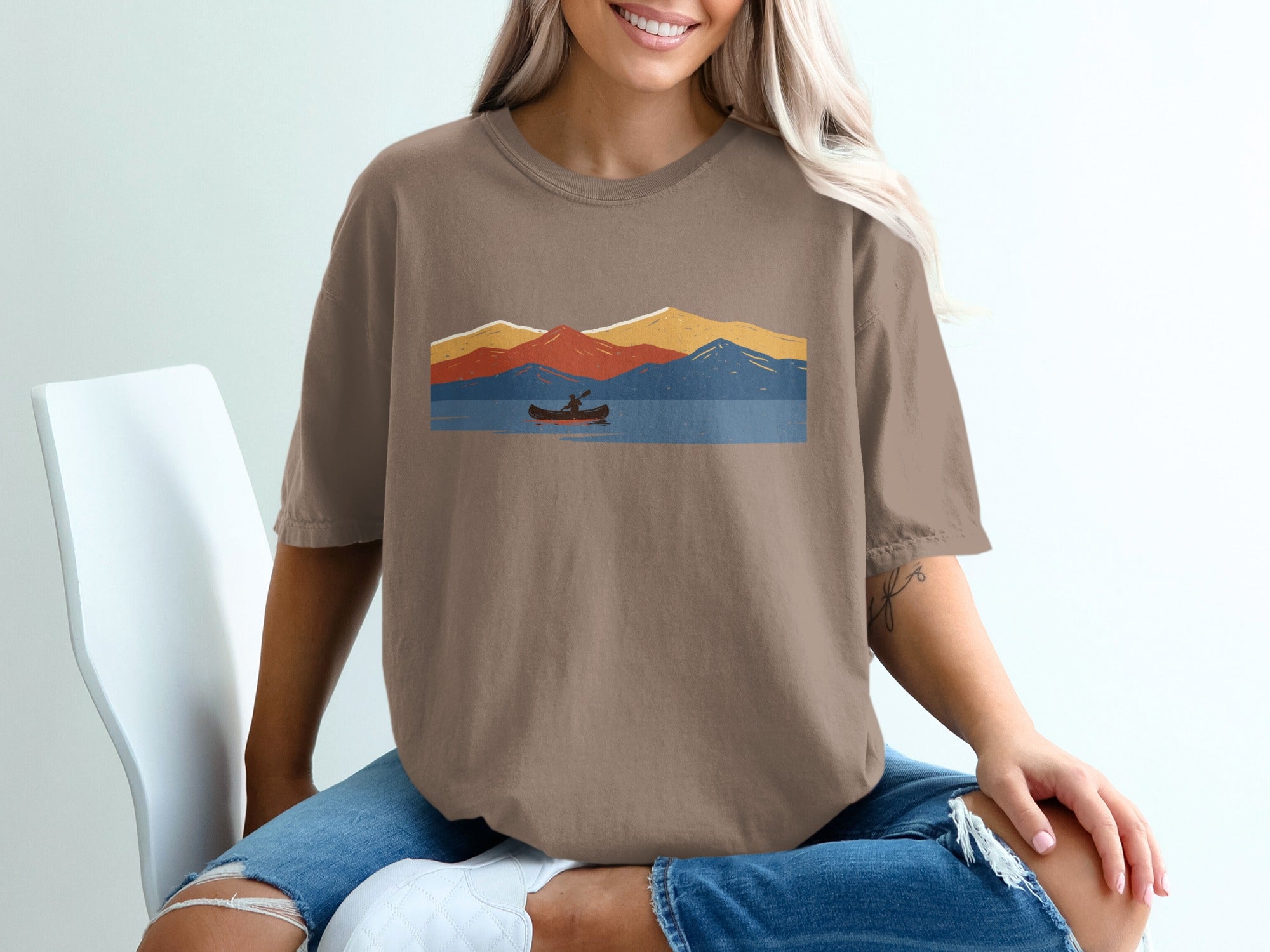 Brown t-shirt with abstract mountains, lake, and canoe graphic.