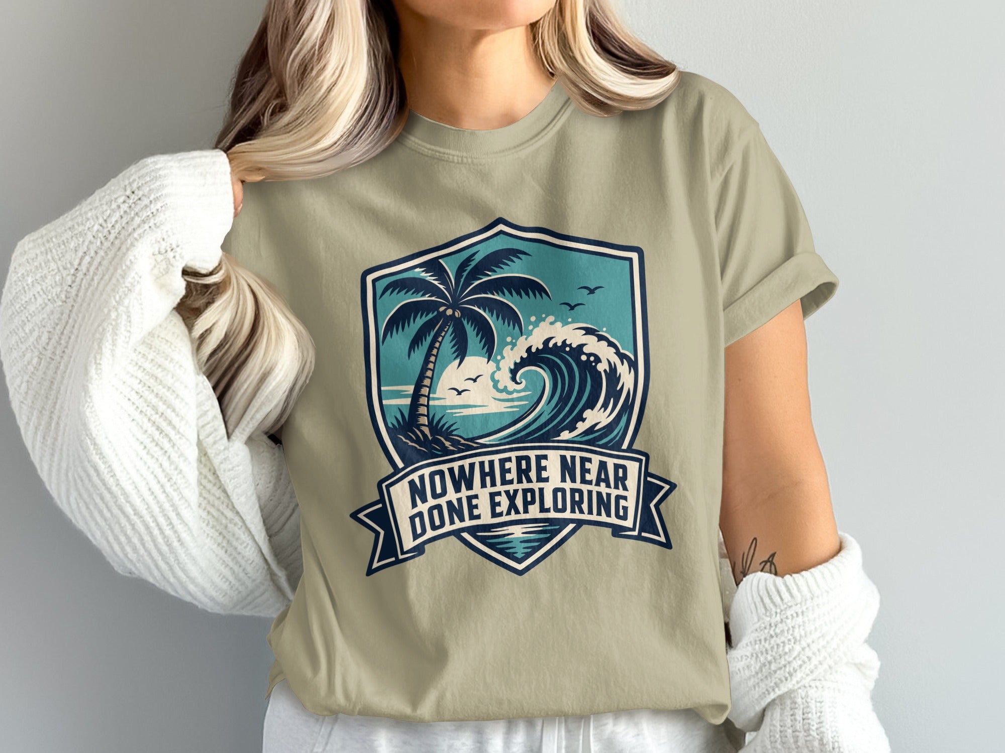 T-shirt with shield graphic featuring palm tree, wave, and text "Nowhere Near Done Exploring".