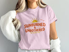 Pink t-shirt with "Sunburned & Unbothered" text and a sunset graphic.