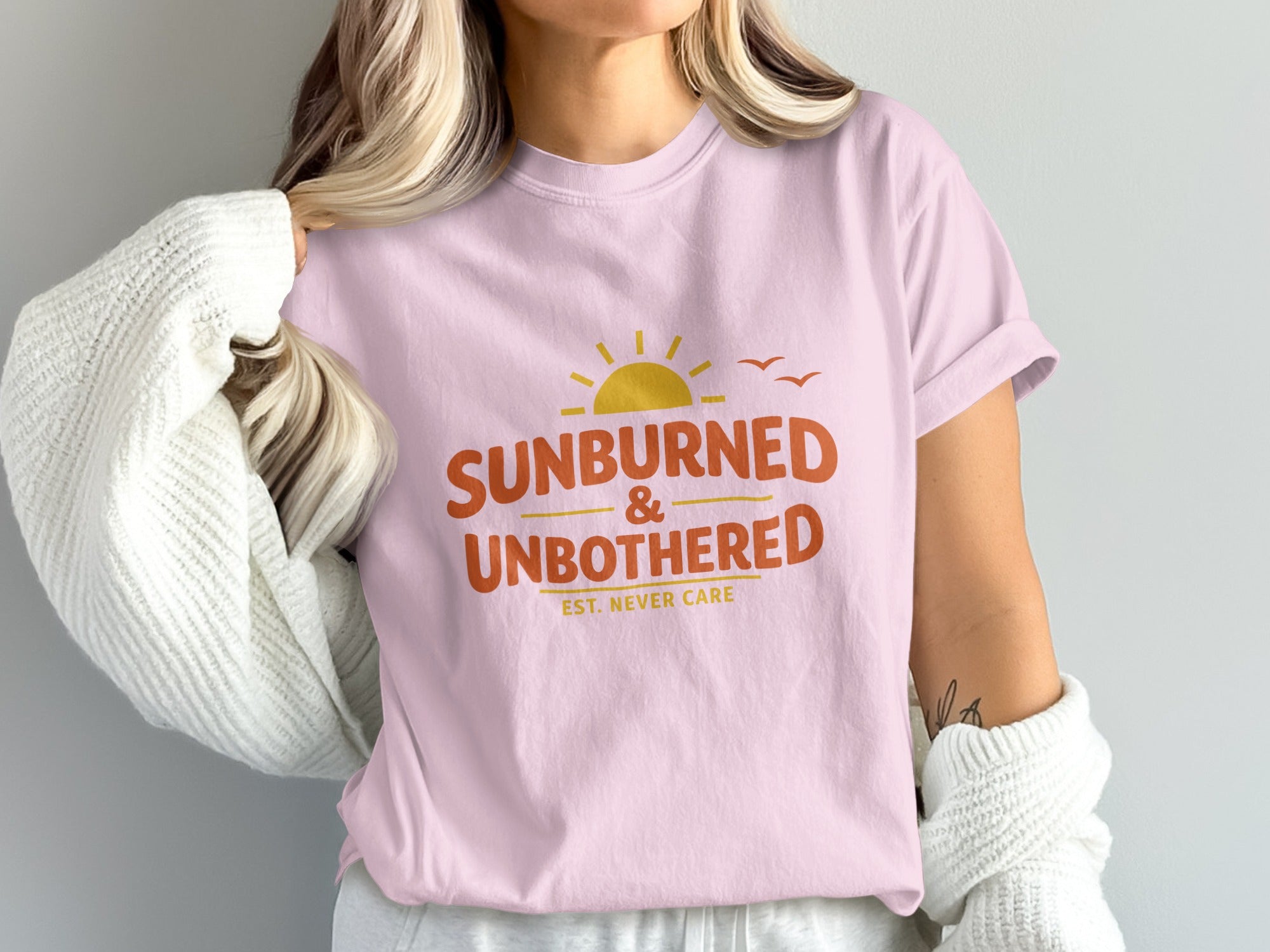 Pink t-shirt with "Sunburned & Unbothered" text and a sunset graphic.