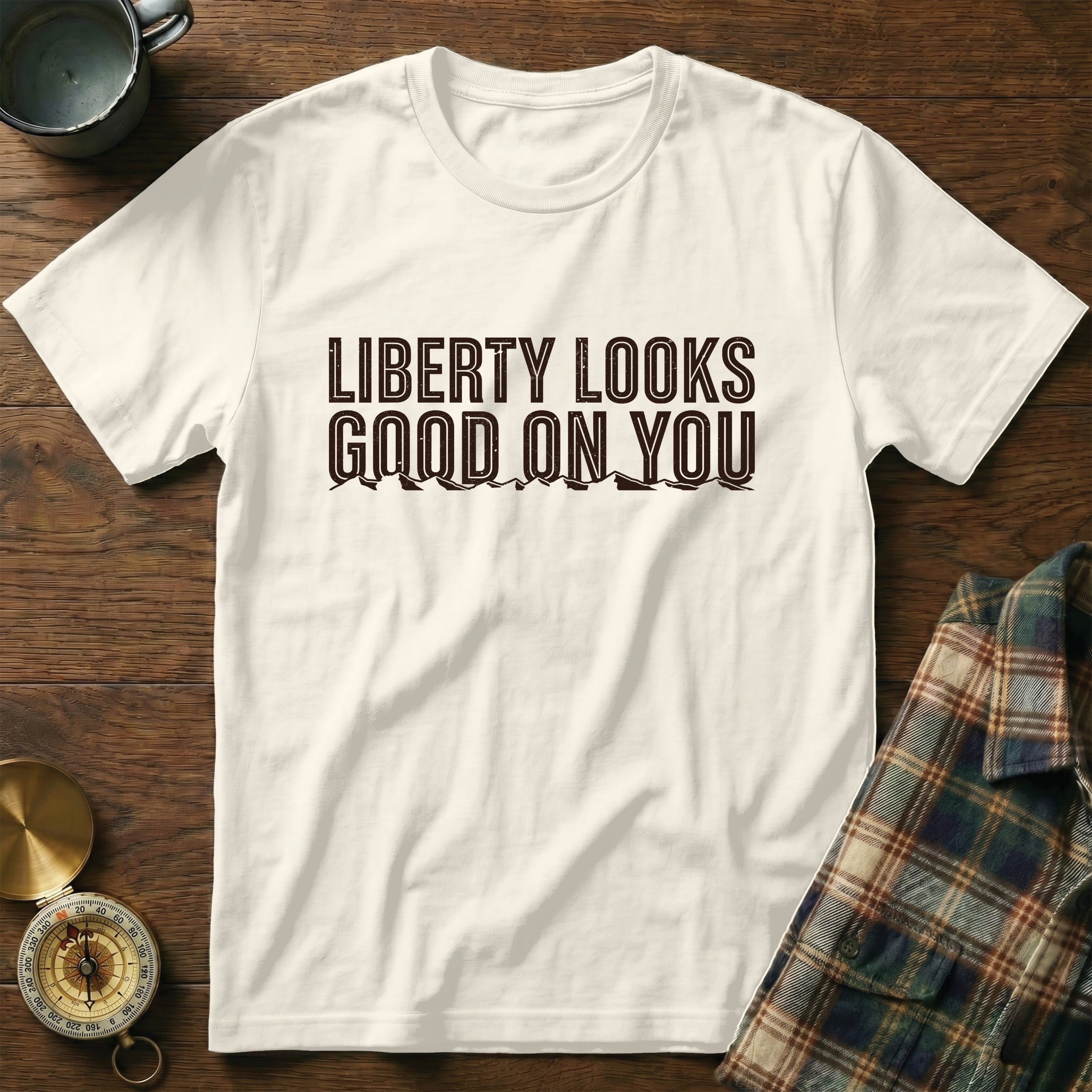 White t-shirt with brown text "Liberty Looks Good On You" and mountain graphic.