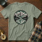 Sage green t-shirt with round mountain forest lake reflection graphic.