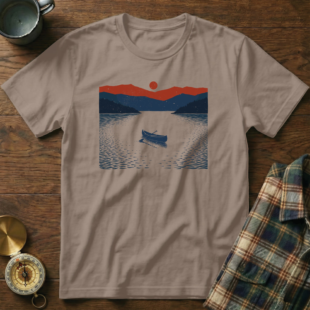T-shirt with a graphic of a rowboat on a lake at sunset with mountains.