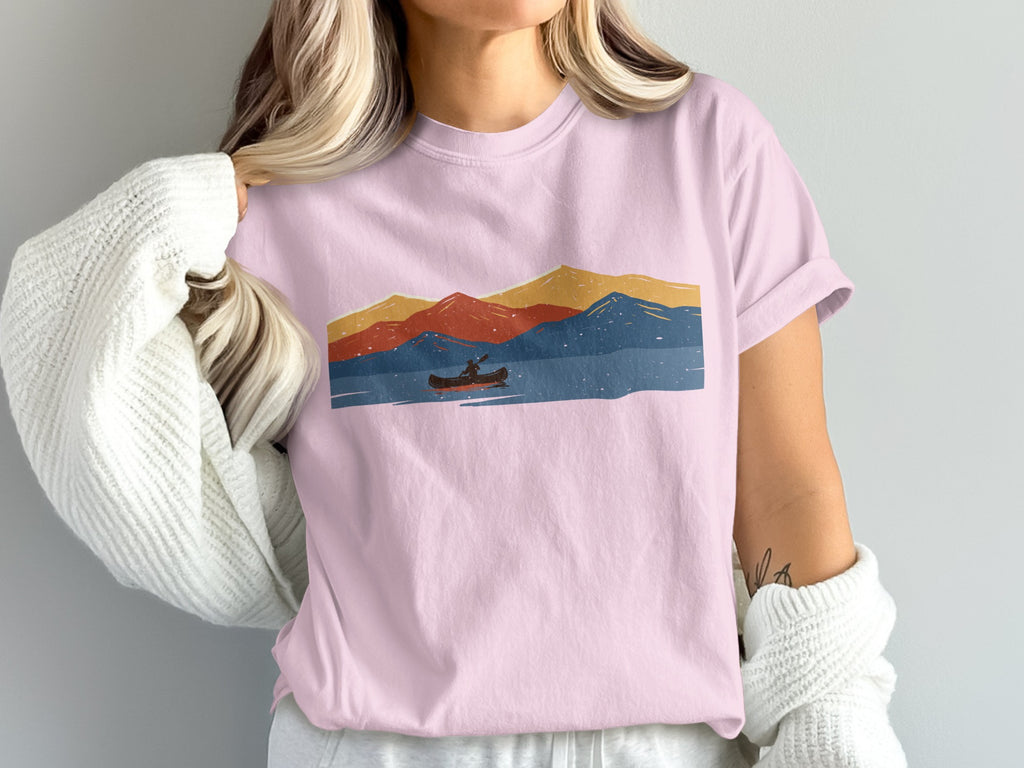 Pink t-shirt with abstract mountain range, lake, and canoe graphic.