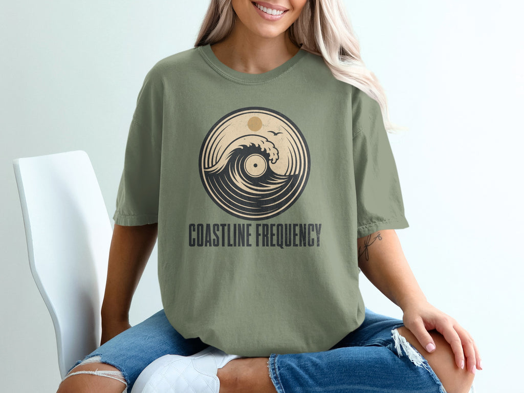 Green t-shirt with circular wave and sun design and "COASTLINE FREQUENCY" text.