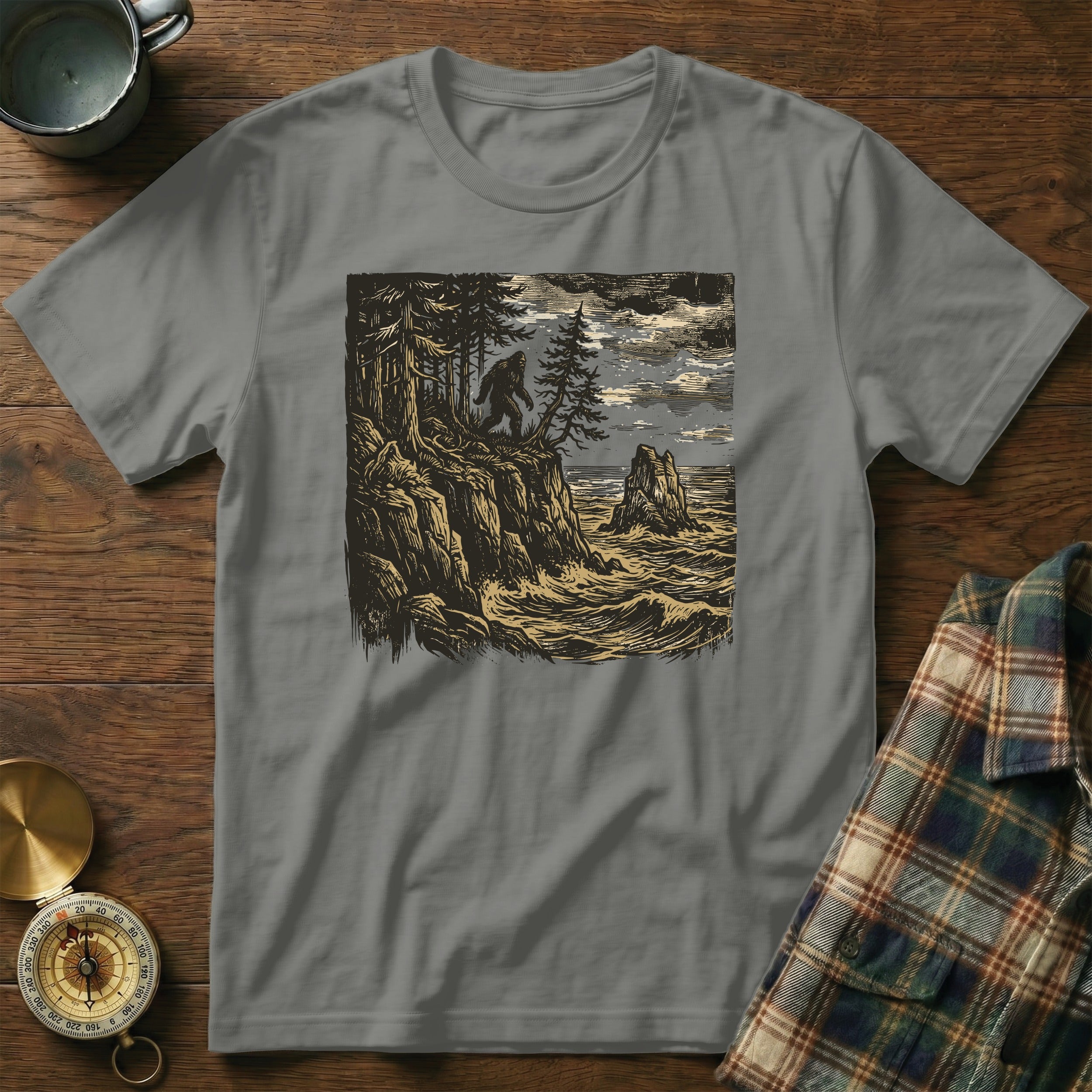T-shirt with Bigfoot graphic on a rocky cliff overlooking the ocean.