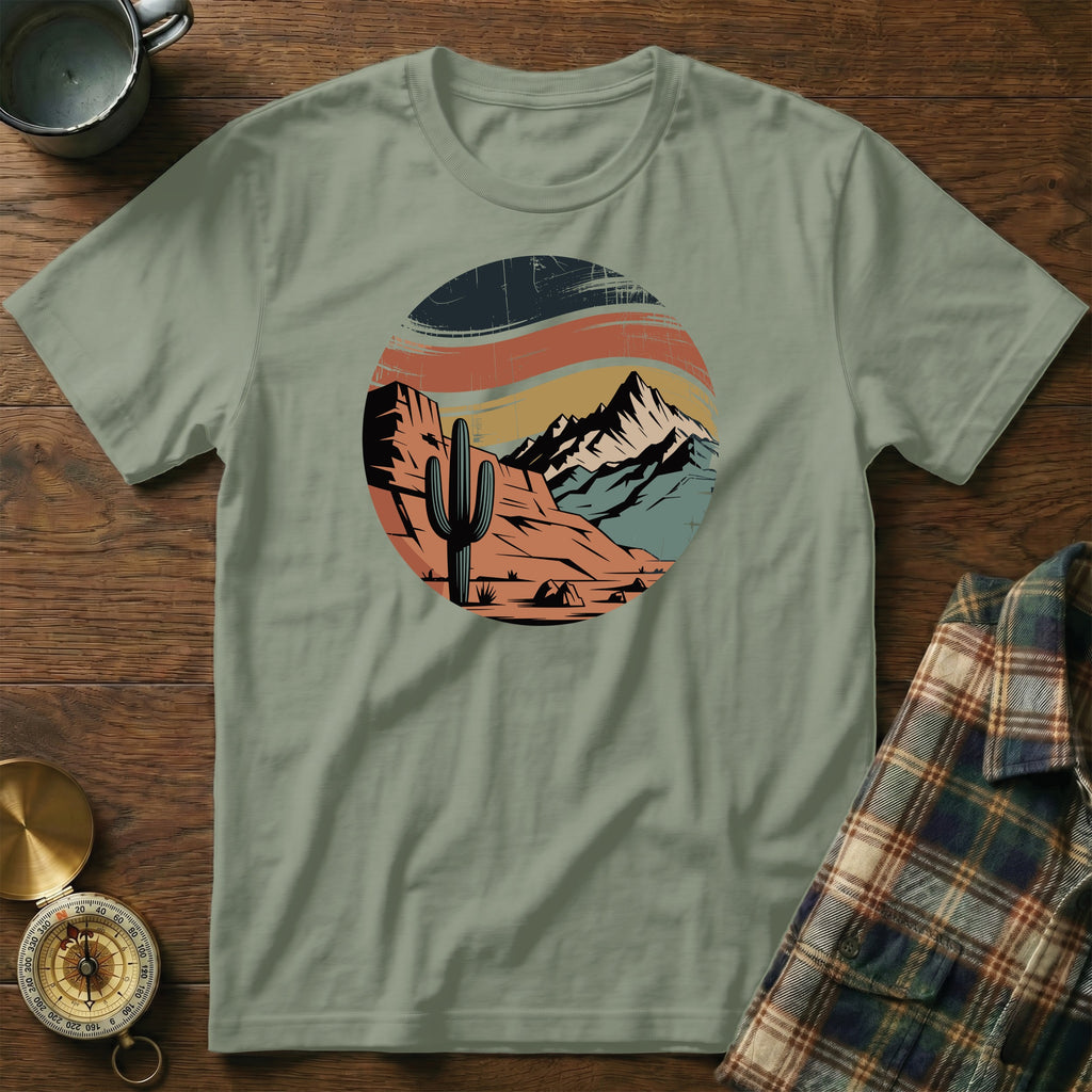 Circular desert landscape graphic with cactus, mountains, and sunset on a sage green t-shirt.