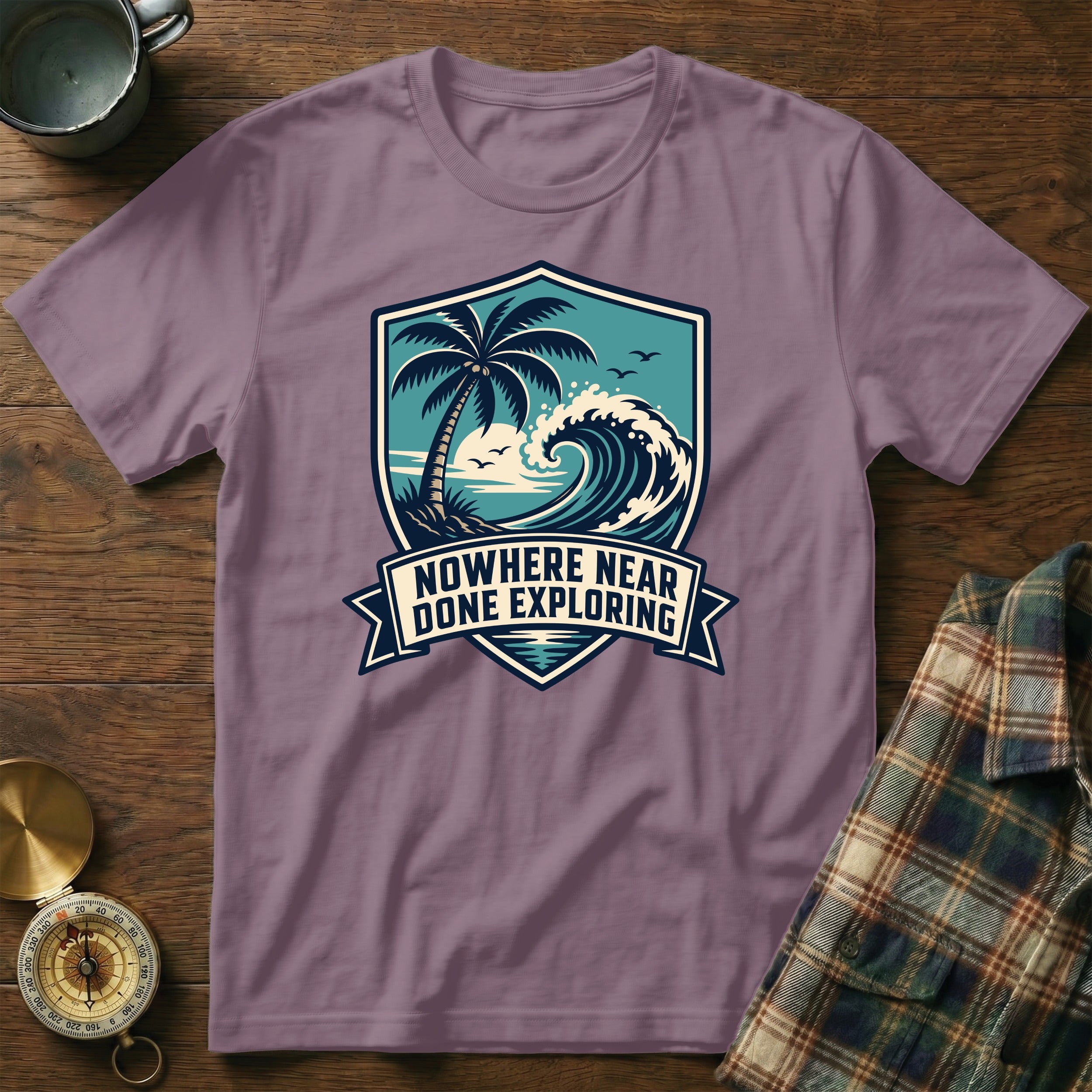 T-shirt with crest design featuring palm tree, wave, and text "Nowhere Near Done Exploring".