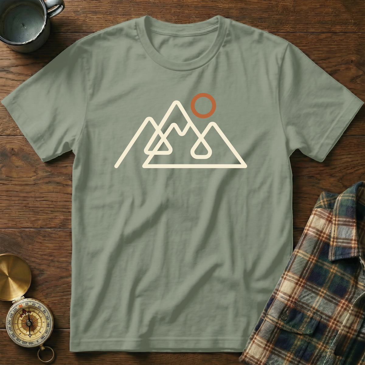 Sage green t-shirt with white outline mountain graphic and orange sun.