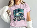 Pink t-shirt featuring a shield graphic with a palm tree, wave, and text.