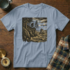 Light blue t-shirt with Bigfoot illustration on rocky coast with waves.