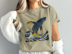 Tan t-shirt with graphic of a blue whale breaching ocean waves.