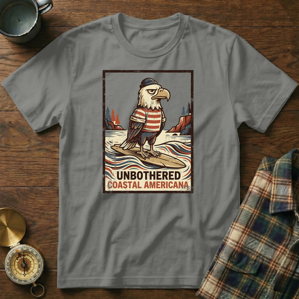 T-shirt with graphic of eagle in striped shirt on surfboard, text "Unbothered Coastal Americana".