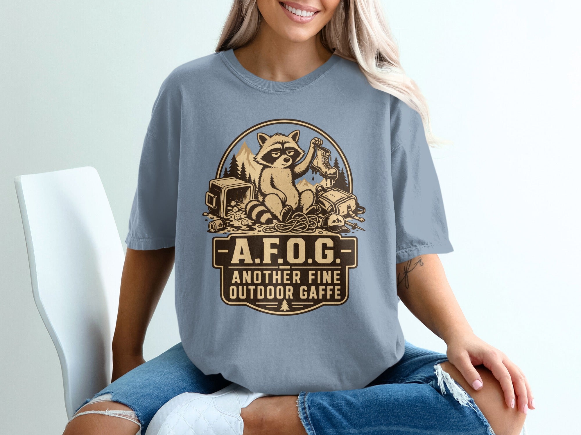 T-shirt graphic of raccoon with boot and camping gear, text: AFOG, Another Fine Outdoor Gaffe.