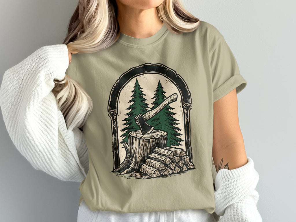 T-shirt graphic of an axe in a tree stump with firewood and pine trees.